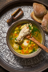 Chicken soup in a clay bowl, bread, wooden spoon, top view