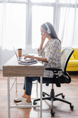 side view of happy freelancer in headphones typing on laptop at home