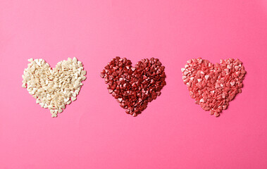 Hearts made with sprinkles on pink background, flat lay