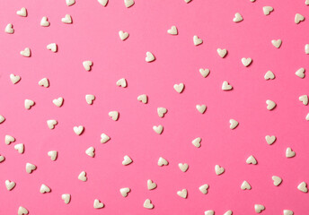 White heart shaped sprinkles on pink background, flat lay