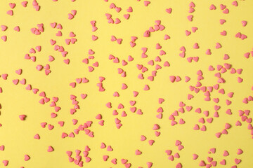 Bright heart shaped sprinkles on yellow background, flat lay