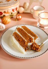 Piece of glazed carrot layer cake on white plate with Christmas seasonal background