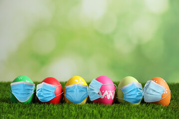 COVID-19 pandemic. Colorful Easter eggs in protective masks on green grass