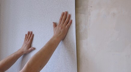 hands smoothing a strip of light non-woven wallpaper on the wall, manually leveling the wallpaper when updating the interior of a room, repairing on our own