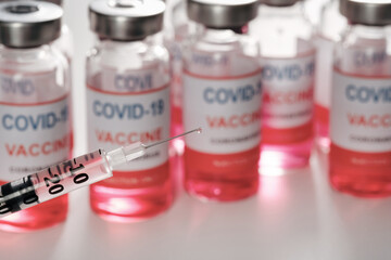 The needle of syringe closeup on blurred vaccine vials to fight the of Covid-19 SARS-CoV-2 coronavirus. Copy space for text 