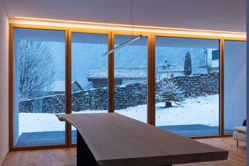 Interior of a dining room, with a large bay window, no one inside and outside there is snow