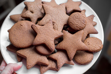 Brown gingerbread in the form of stars are piled on a white plate.