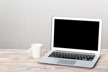 Fototapeta premium Laptop with blank screen for product display and white cup on a wooden table. work from home
