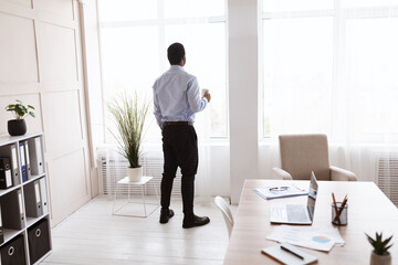 African american businessman drinking coffee near window, back view