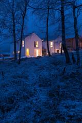 Modern white house with light windows surronded by mountain, snow and trees. Chirstmas mood