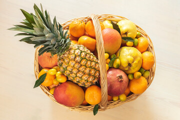 A basket of tropical fruits: pineapple, mango, grapefruit, tangerines, oranges, pomegranates, kumquat on a white background