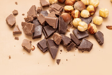 Broken chocolate pieces and hazelnuts on beige background