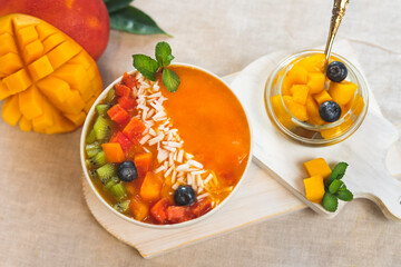 Naklejka na ściany i meble Fresh fruit breakfast. Smoothie bowl of mango, papaya on the table, decorated with pieces of kiwi, blueberry berries and mint leaf