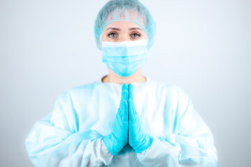 a nurse in a medical gown, mask, and protective gloves clasped her hands in front of her in a gesture of supplication