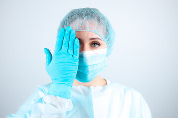 a nurse in a medical gown, mask, and protective gloves covered her eyes with her hands