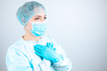 a nurse in a medical gown, mask, and protective gloves stands sideways with her arms crossed over her chest