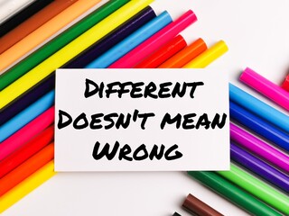 Text DIFFERENT DOES NOT MEAN WRONG on paper note with colorful pencils isolated on white background.Motivational quote.