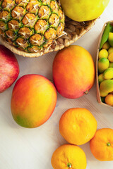 Mango close-up among tropical fruits, tangerines, kumquat, pineapple and pomegranate on white background