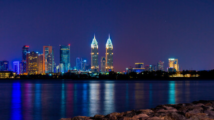 Night view to iconic skyscrapers panorama of Dubai. Amazing illumination of the Business Central Towers. Luxury skyscrapers represent modern Dubai. Colors reflect over water.