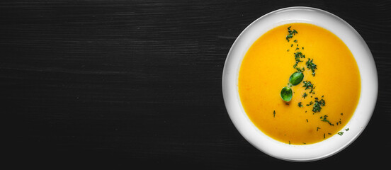 Pumpkin soup in white plate on black wooden table background