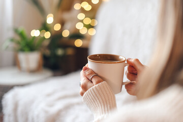 Woman's hands in sweater holding cup of hot drink coffee indoors. Still life composition.