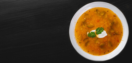 Soup with pickled cucumbers and pearl barley in white plate on black wooden table background