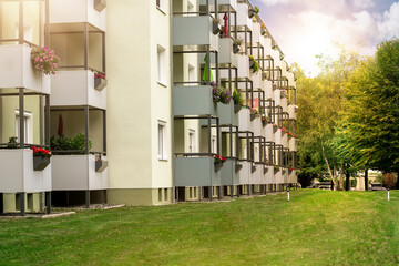 Mehrfamilienhaus mit Balkon, Blumen, Rasenflächen und Bäumen im Vorgarten und Hintergarten.