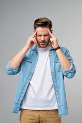 Frustrated young caucasian man in jeans shirt touching head with hand while standing overg studio grey background