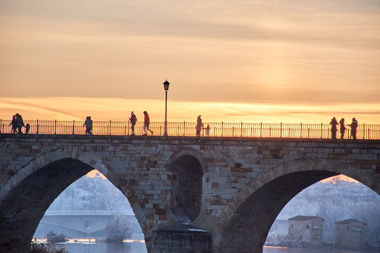 People walking on a stone bridge at sunset and the frozen trees in winter at the golden hour