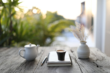 small back tea cup and white kettle and dry flower vase and notebook on wooden table