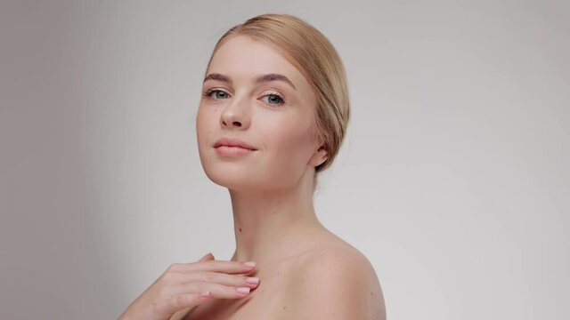 Close up beauty portrait of young woman touching her smooth skin in collarbone area. Skin care concept. Female model with fresh skin, white smile and natural facial makeup portrait. Slow motion.