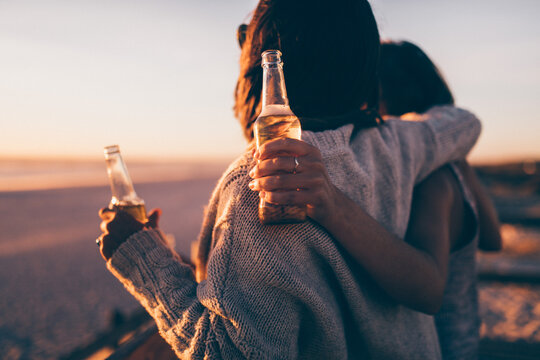 Close-up of women holding bottle of beer at beach