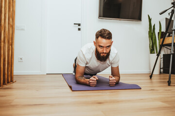 Young man making sport fitness exercises at home. Training during quarantine. Online training in front of the smartphone camera.