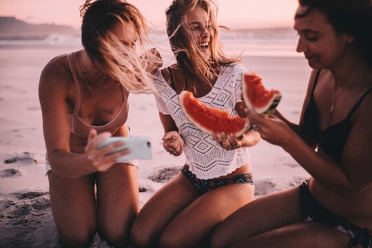 Female caucasian friends eating watermelon at the beach
