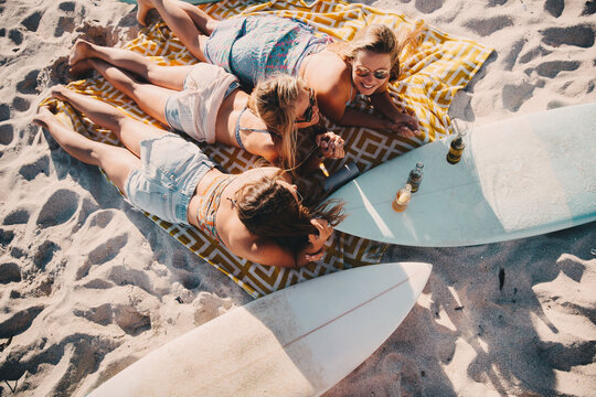 Young adult women friends laying on the beach together with surfboards
