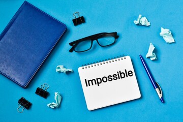 IMPOSSIBLE. Notebook with pen, glasses and crumpled paper on a blue background. Business concept.