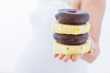 Pregnant woman choosing between donuts and slices of pineapple