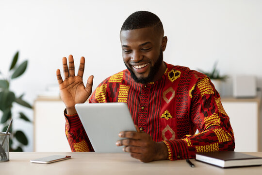 Cheerful black guy in african shirt making video call with digital tablet