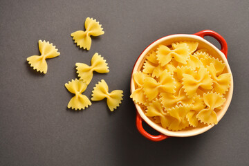 Directly above of red cooking pot with uncooked italian farfale pasta with scattered pasta pieces on dark background
