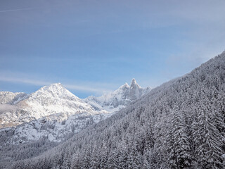 heavy snow covers the mountains and tress of Chamonix in France. A cross country skier carves a path through the deep snow in the forest on a perfect winter day.