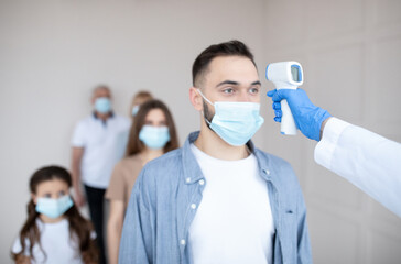 Medical worker checking young man's temperature with infrared thermometer at hospital. Coronavirus...
