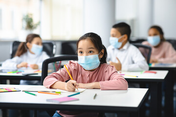 Asian girl in mask sitting at desk in classroom