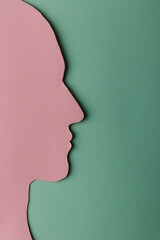 Head silhouette made of paper. Pink paper shaped as a human head with copy space on green paper background.