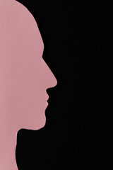Head silhouette made of paper. Pink paper shaped as a human head with copy space on black paper background.