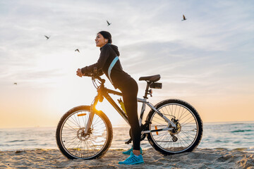 Fototapeta na wymiar young attractive slim woman riding bicycle, sport on morning sunrise summer beach in sports fitness wear, active healthy lifestyle, smiling happy having fun
