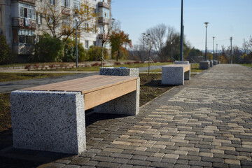 Obraz premium In the park there is a wooden bench with a back, with marble legs and a marble trash can.Outdoor bench made of wood and marble.White marble trash can with a metal surface inside. Wooden bench for rest