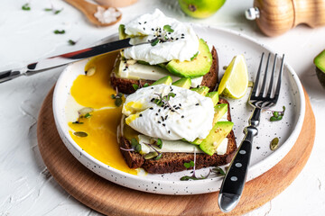 Tasty sandwich with avocado and poached egg on wooden chopping board, Healthy delicious breakfast...