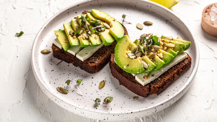 Healthy avocado toasts for breakfast or lunch with rye bread, sliced avocado, cheese, pumpkin and sesame seeds. banner, catering menu recipe top view