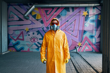Graffiti painter in respirator mask standing near the wall with his paintings