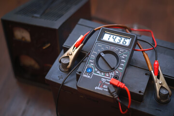 Checking voltage with multimeter and charging car battery with charger from home electricity. Recovery of acid batteries, resuscitate car battery. Voltmeter to check voltage level on car battery